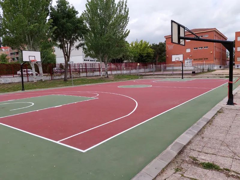 Construcción de cancha de baloncesto en colegio de Madrid. Cancha de baloncesto exterior en un colegio de Madrid, con suelo de color rojo y verde, líneas blancas y varias canastas.