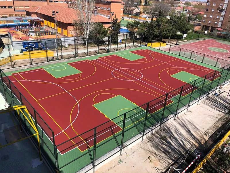 Instalación deportiva con pavimento de resina en colores rojo y verde, delimitadas con valla de seguridad.